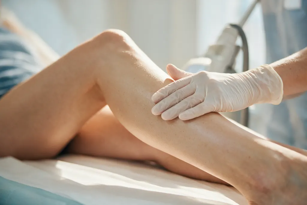 A gloved hand guiding a laser handpiece along a leg